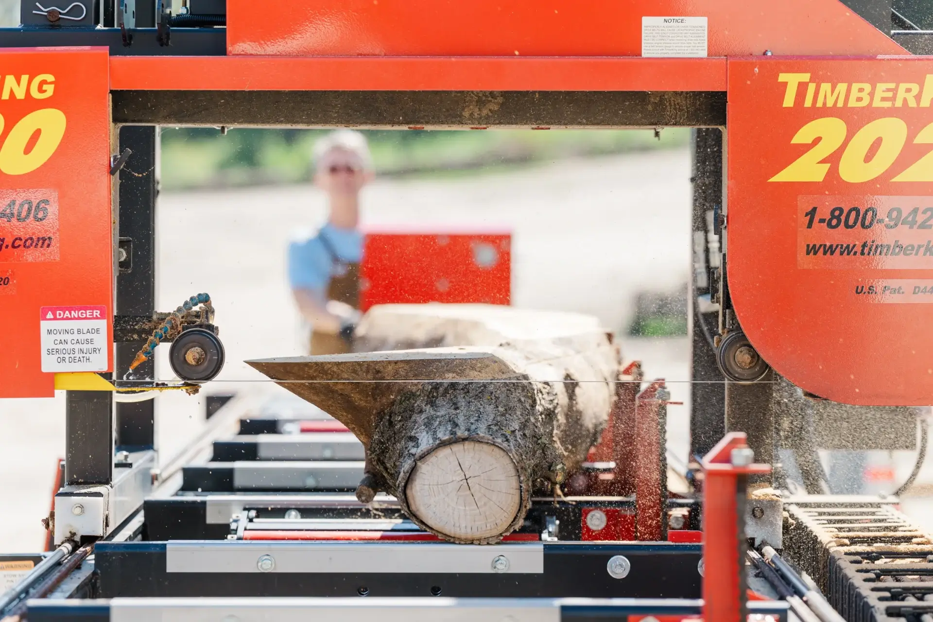 A log being cut by a red sawmill machine outdoors.