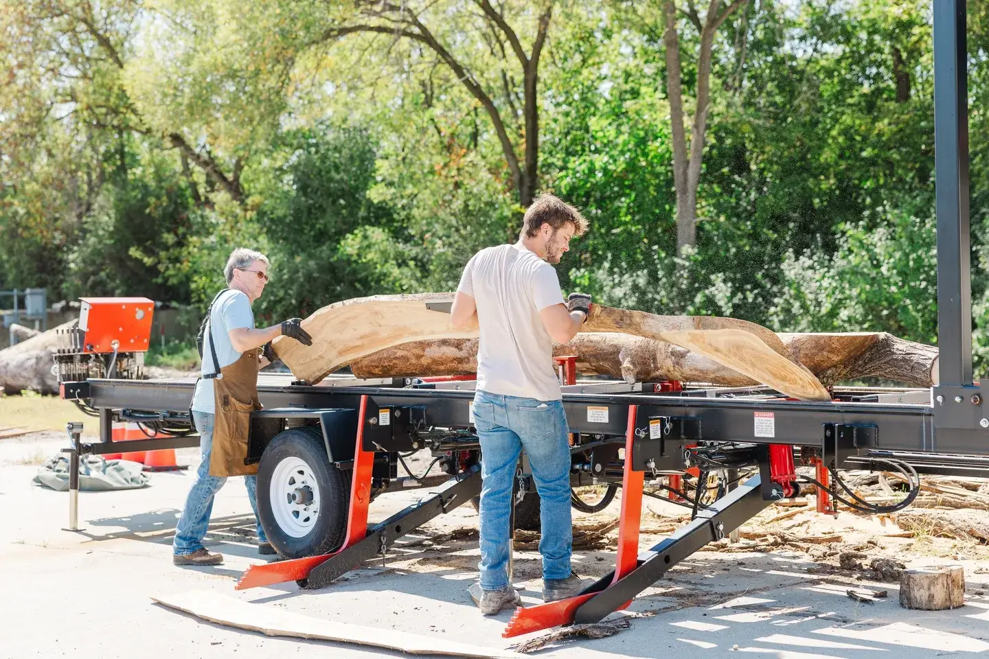 Two men shaping a large wooden canoe outdoors.