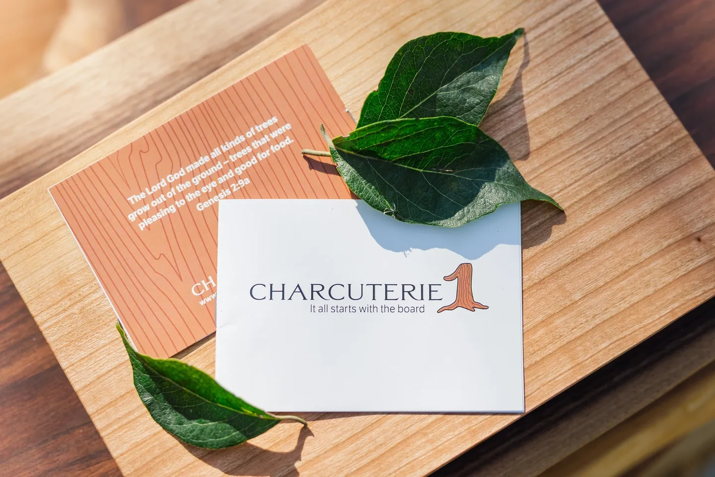 A business card for Charcuterie 1 on a wooden surface with green leaves.
